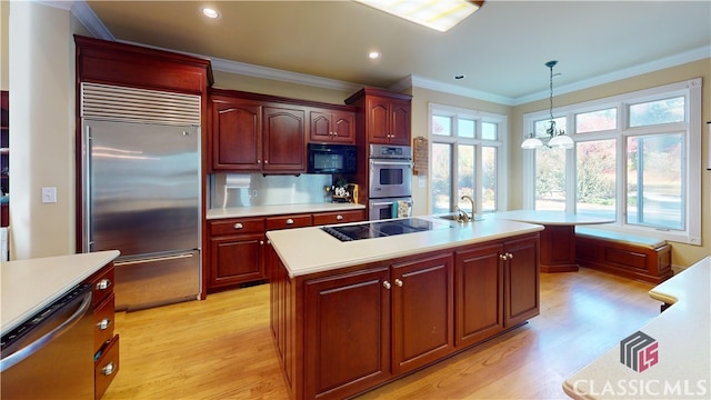 kitchen with light hardwood / wood-style flooring, decorative light fixtures, a kitchen island with sink, and black appliances