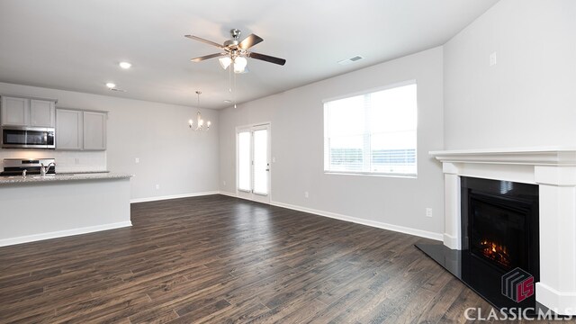 unfurnished living room with dark wood-type flooring and ceiling fan with notable chandelier