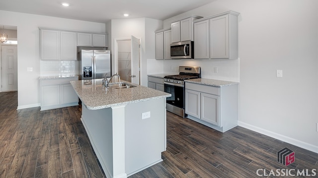 kitchen with dark wood-type flooring, appliances with stainless steel finishes, sink, and an island with sink