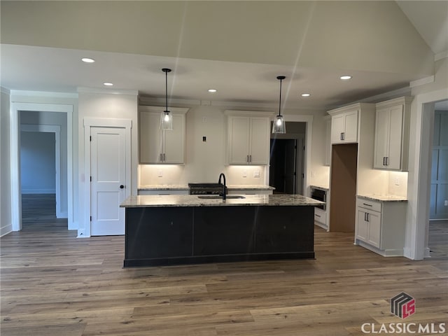 kitchen featuring stone counters, sink, a center island with sink, and decorative light fixtures