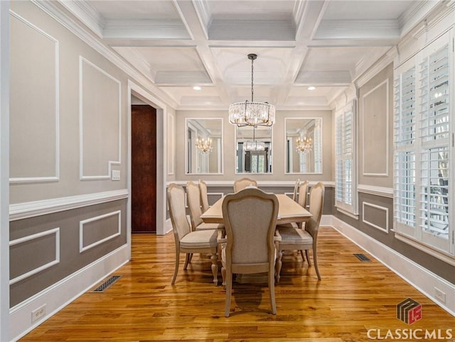 dining area with a decorative wall, a chandelier, beam ceiling, wood finished floors, and crown molding