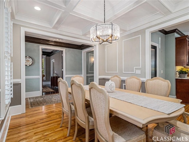 dining room with a chandelier, ornamental molding, light wood finished floors, a decorative wall, and coffered ceiling