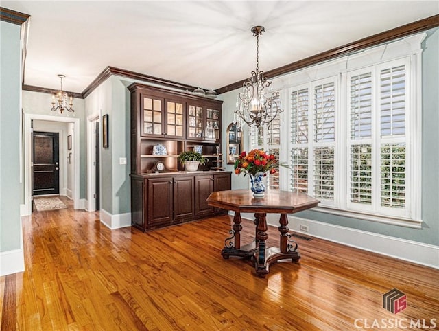 dining space with a chandelier, crown molding, baseboards, and wood finished floors