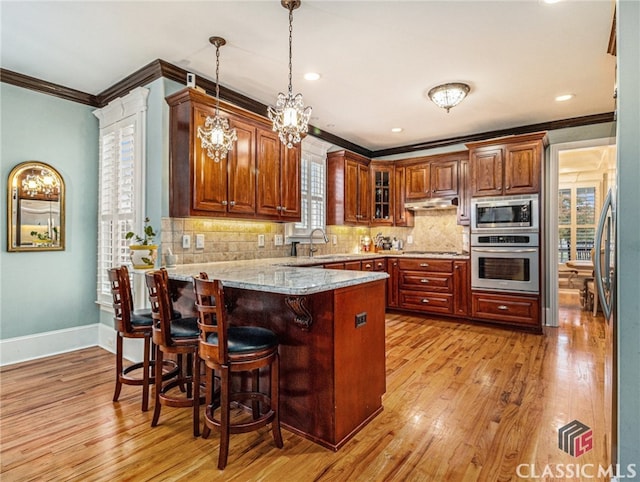 kitchen with kitchen peninsula, appliances with stainless steel finishes, ornamental molding, light hardwood / wood-style flooring, and hanging light fixtures