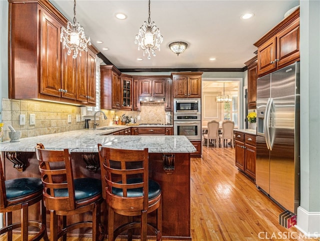 kitchen with kitchen peninsula, appliances with stainless steel finishes, crown molding, an inviting chandelier, and light hardwood / wood-style floors