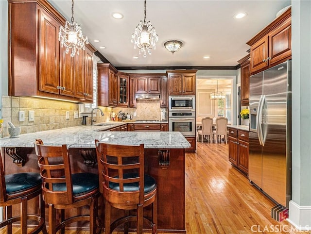 kitchen with appliances with stainless steel finishes, a chandelier, a sink, a peninsula, and pendant lighting
