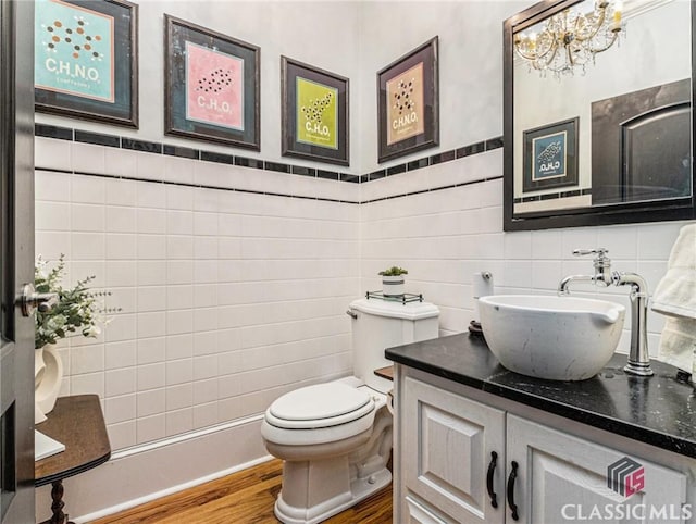 half bath featuring wood finished floors, tile walls, a chandelier, toilet, and vanity