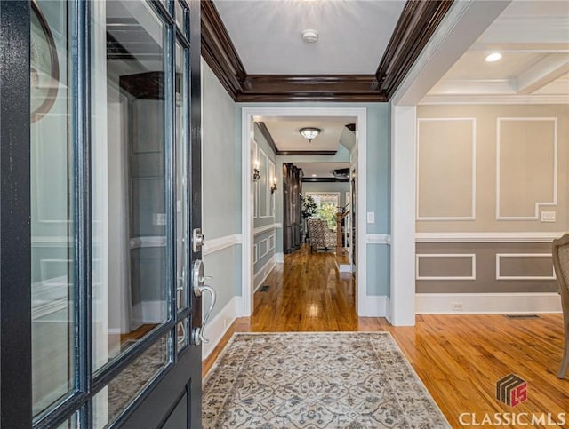 foyer entrance featuring crown molding, wood finished floors, a decorative wall, and baseboards