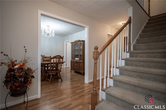 staircase featuring a textured ceiling, wood-type flooring, and an inviting chandelier