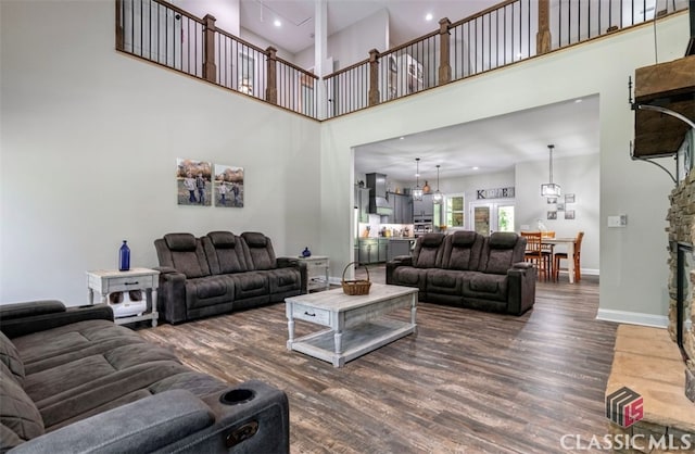 living room with a towering ceiling, wood-type flooring, and a stone fireplace