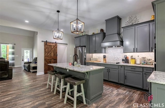 kitchen featuring high quality fridge, pendant lighting, a barn door, custom range hood, and a center island with sink