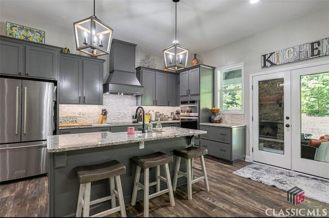 kitchen featuring pendant lighting, stainless steel appliances, an island with sink, and premium range hood