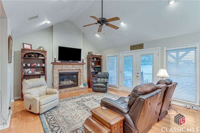 living room featuring a brick fireplace, french doors, high vaulted ceiling, ceiling fan, and light wood-type flooring