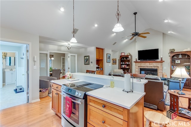 kitchen featuring a kitchen island, stainless steel electric range oven, a brick fireplace, lofted ceiling, and light hardwood / wood-style flooring