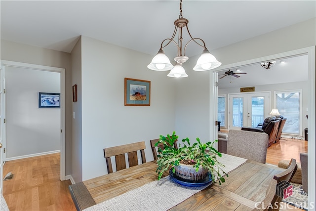 dining room with ceiling fan with notable chandelier, light wood-type flooring, and french doors