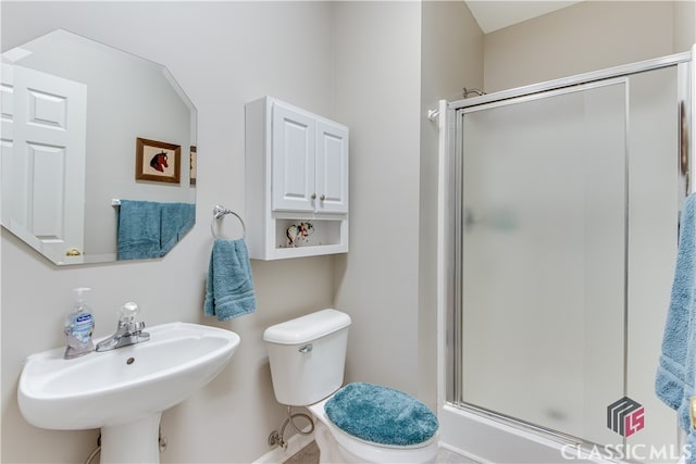 bathroom featuring toilet, sink, and a shower with shower door