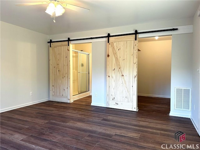 unfurnished bedroom featuring a barn door, ceiling fan, and dark wood-type flooring