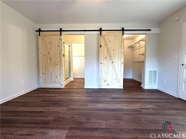 unfurnished bedroom with a barn door, dark hardwood / wood-style flooring, a spacious closet, and a closet