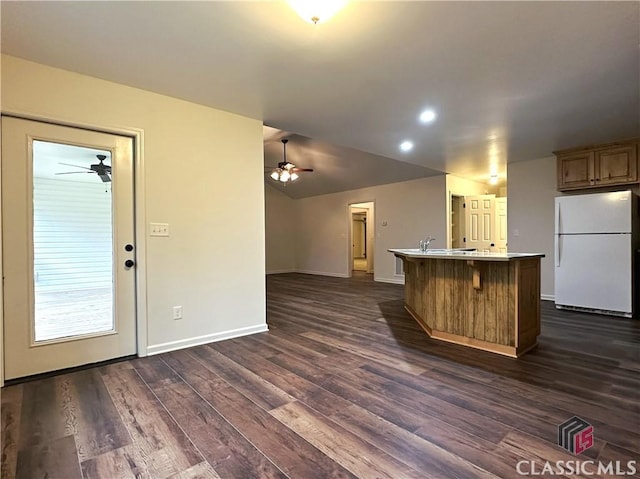 kitchen with white fridge, dark hardwood / wood-style floors, a breakfast bar area, and an island with sink