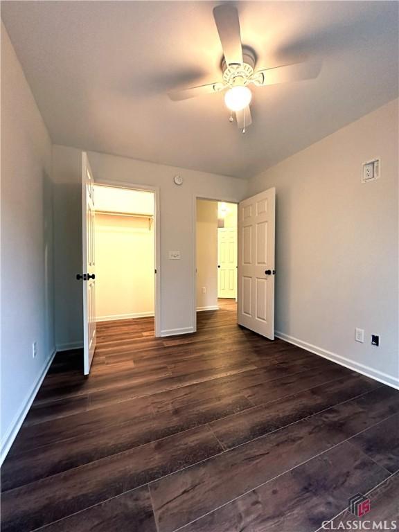 unfurnished bedroom featuring ceiling fan, a spacious closet, dark wood-type flooring, and a closet