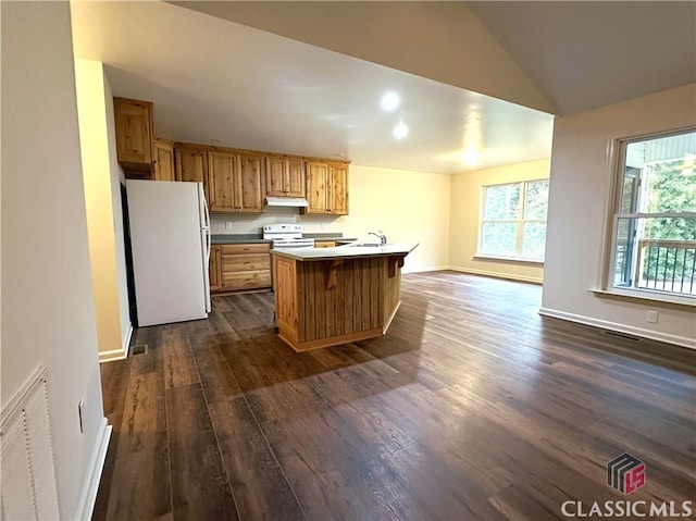 kitchen with sink, dark hardwood / wood-style flooring, white appliances, a breakfast bar, and a kitchen island