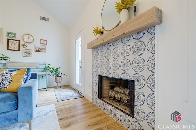 living room with lofted ceiling, a tile fireplace, light hardwood / wood-style floors, and plenty of natural light