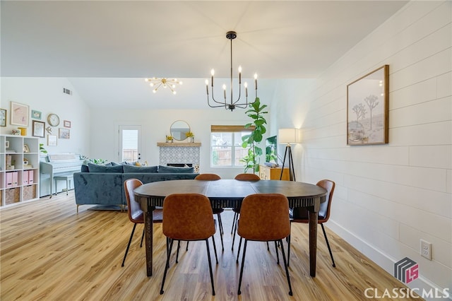 dining space featuring a fireplace, light hardwood / wood-style floors, an inviting chandelier, and vaulted ceiling