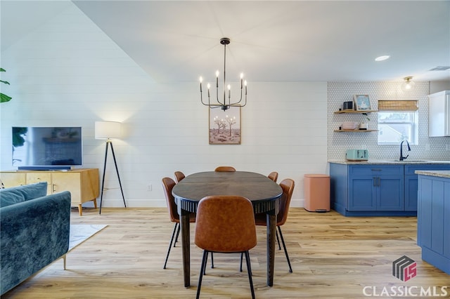 dining room with an inviting chandelier, wooden walls, sink, and light hardwood / wood-style flooring