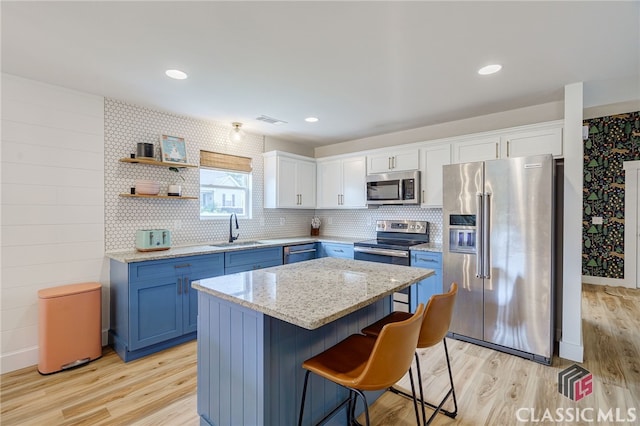 kitchen with stainless steel appliances, sink, light hardwood / wood-style flooring, a kitchen island, and white cabinets