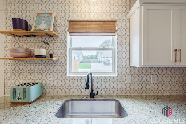 kitchen featuring white cabinetry, sink, light stone counters, and backsplash