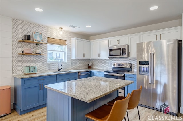 kitchen with sink, blue cabinetry, a kitchen island, white cabinetry, and appliances with stainless steel finishes