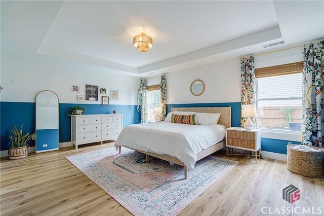 bedroom with multiple windows, light hardwood / wood-style flooring, and a tray ceiling