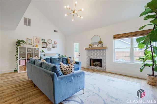 living room with a tile fireplace, light wood-type flooring, high vaulted ceiling, and a notable chandelier