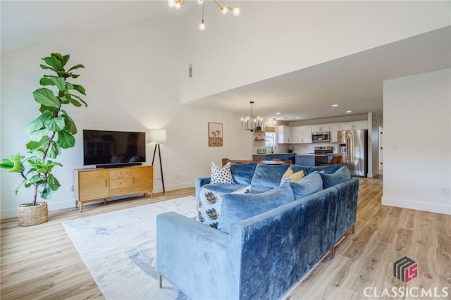 living room with light wood-type flooring, a chandelier, and high vaulted ceiling