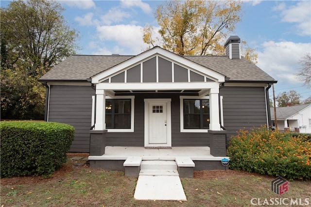 bungalow-style home with a chimney, a porch, and roof with shingles