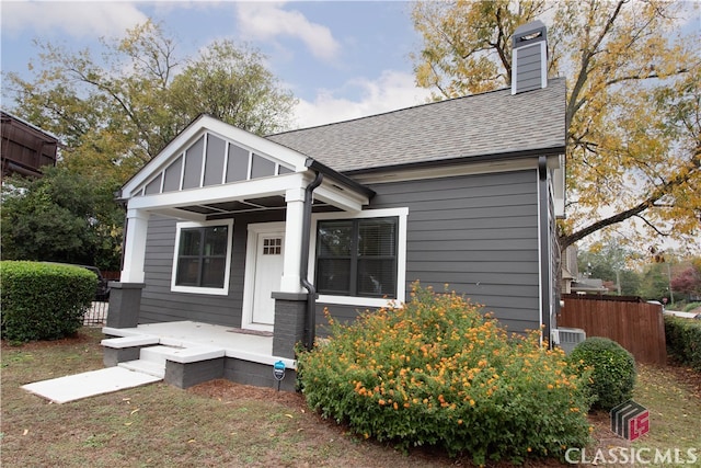 bungalow-style home featuring a shingled roof, a porch, a chimney, and fence