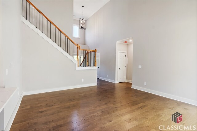 unfurnished living room featuring dark hardwood / wood-style flooring, a towering ceiling, and a chandelier