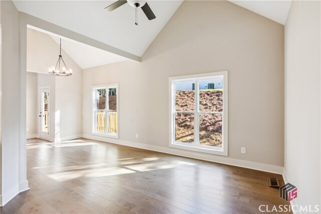 empty room with hardwood / wood-style floors, plenty of natural light, ceiling fan with notable chandelier, and high vaulted ceiling