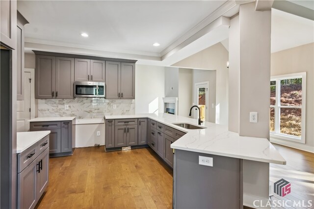 kitchen featuring backsplash, sink, light stone countertops, light wood-type flooring, and kitchen peninsula