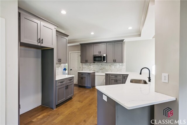 kitchen with kitchen peninsula, decorative backsplash, light hardwood / wood-style floors, and sink