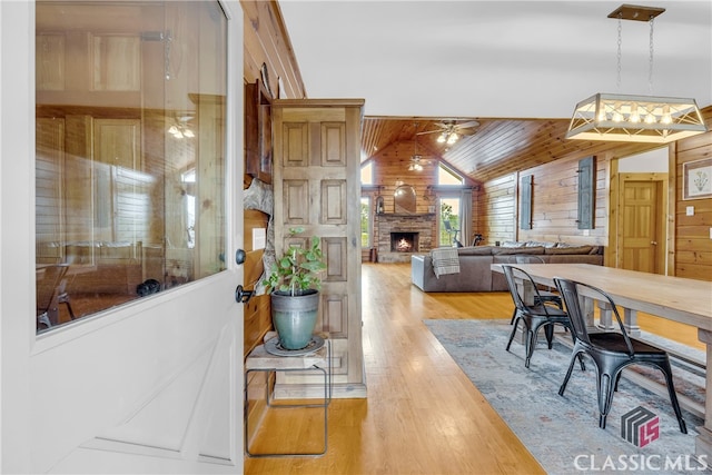 dining room featuring vaulted ceiling, a stone fireplace, wooden walls, wood-type flooring, and wood ceiling