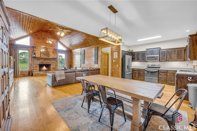 dining area with wooden walls, a fireplace, sink, ceiling fan, and light wood-type flooring