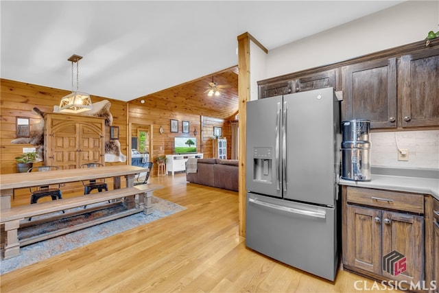 kitchen with stainless steel refrigerator with ice dispenser, wood walls, dark brown cabinets, light hardwood / wood-style flooring, and pendant lighting