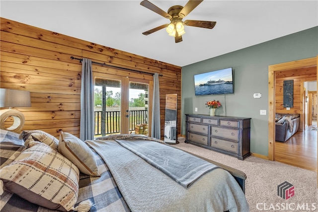 bedroom with access to outside, light colored carpet, ceiling fan, and wood walls