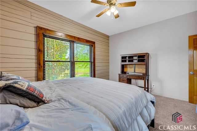 carpeted bedroom featuring ceiling fan and wood walls