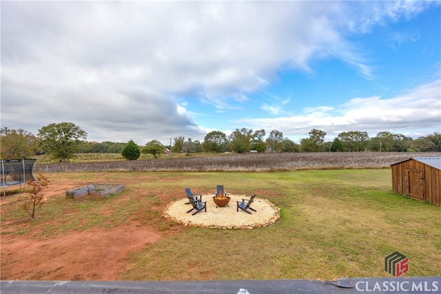 view of yard with a trampoline, a storage unit, a fire pit, and a rural view