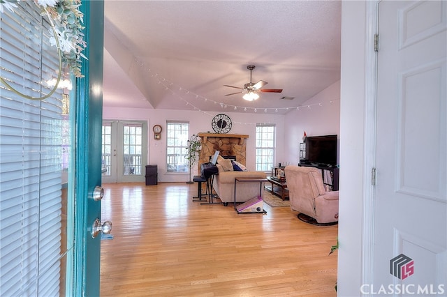 living room featuring ceiling fan, light hardwood / wood-style flooring, vaulted ceiling, a textured ceiling, and a fireplace