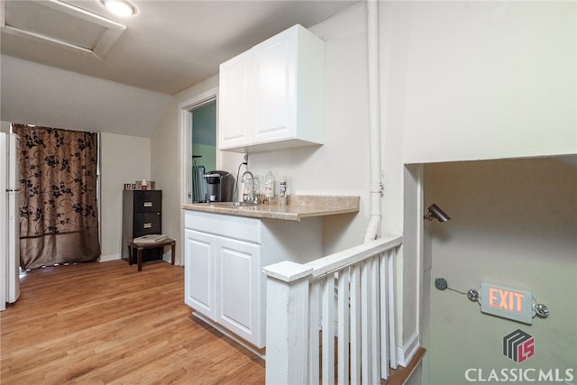 kitchen featuring vaulted ceiling, white cabinetry, sink, and light hardwood / wood-style floors