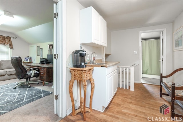 kitchen with sink, white cabinets, vaulted ceiling, and light hardwood / wood-style flooring