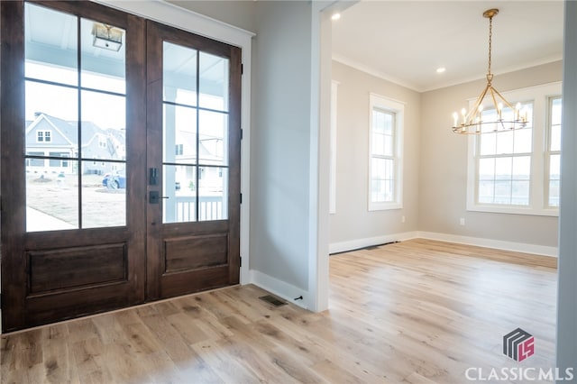 entrance foyer featuring french doors, light wood-type flooring, an inviting chandelier, and crown molding